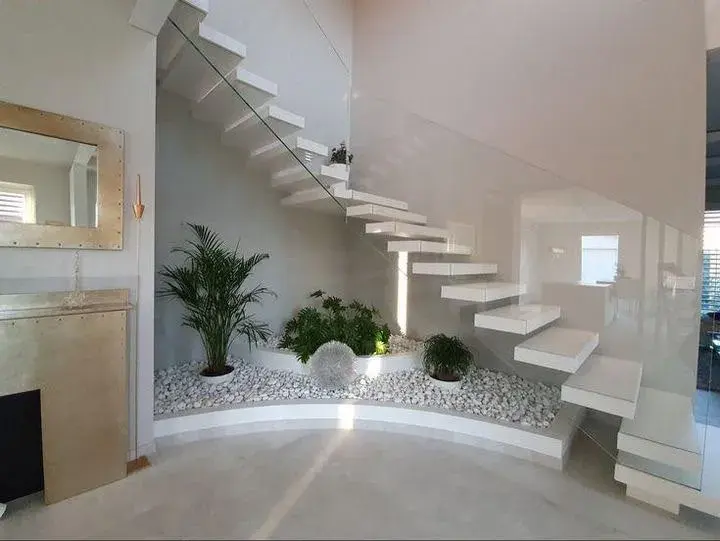 Indoor garden with white pebbles under a floating staircase