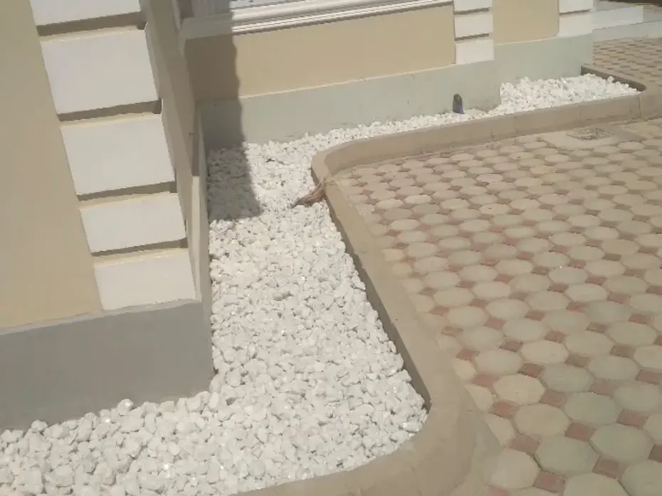 Garden bed filled with white decorative stones beside paving